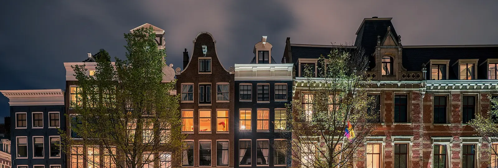 Amsterdam canal houses at night, lit windows reflected in the water.